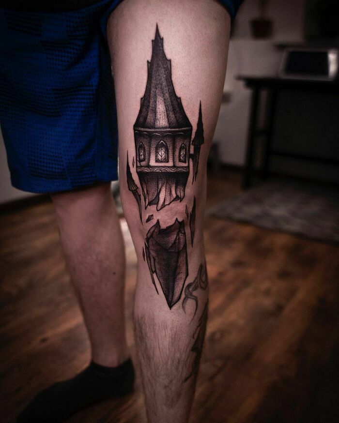 Leg with a detailed black ink knee tattoo design featuring a gothic tower.
