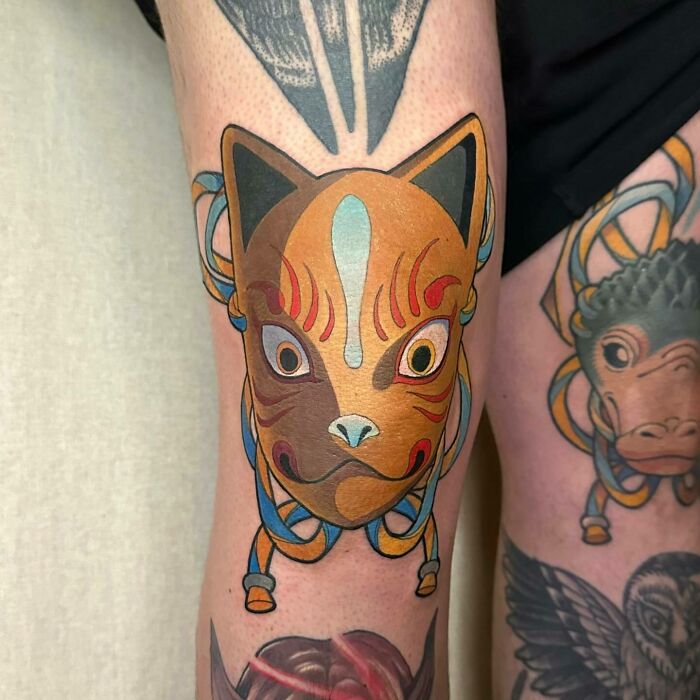 Fox mask knee tattoo design with vibrant colors on a person's leg.