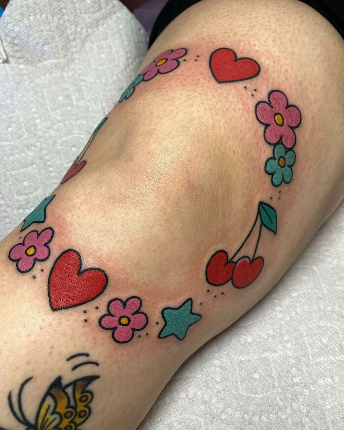 Colorful knee tattoo with hearts, flowers, stars, and cherries design.