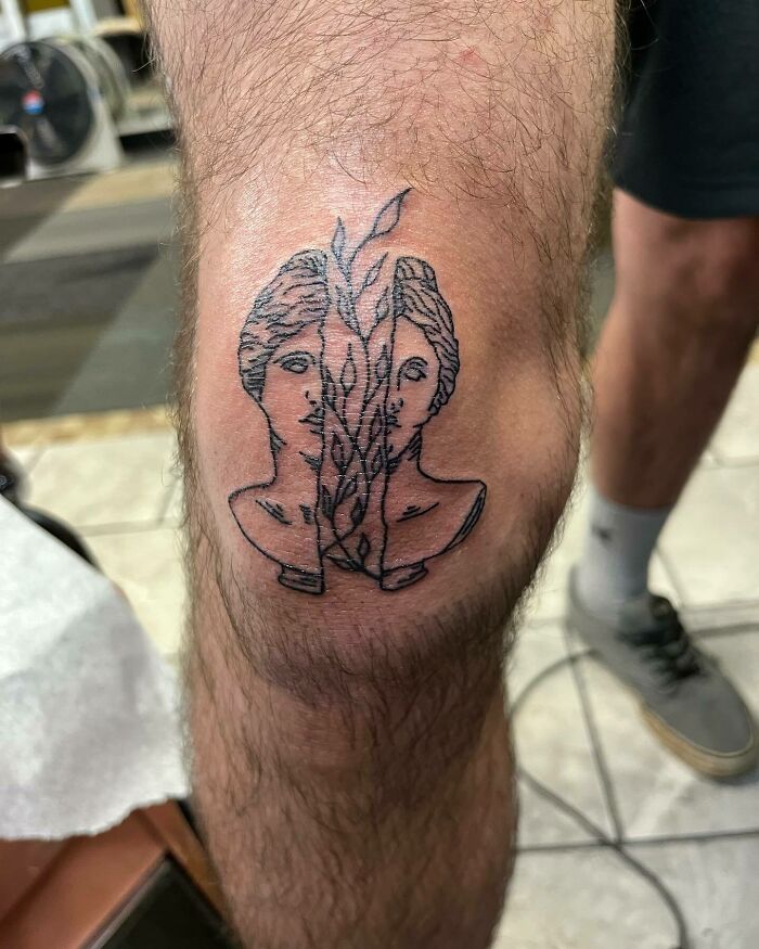 Man with artistic knee tattoo design featuring two faces and leaves.