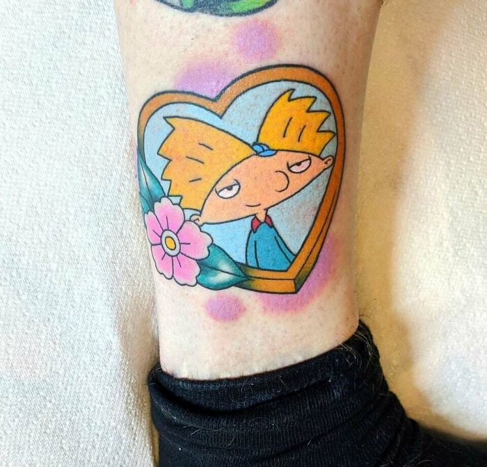 Heart-shaped '90s tattoo featuring a cartoon character with a flower, reflecting nostalgic culture.