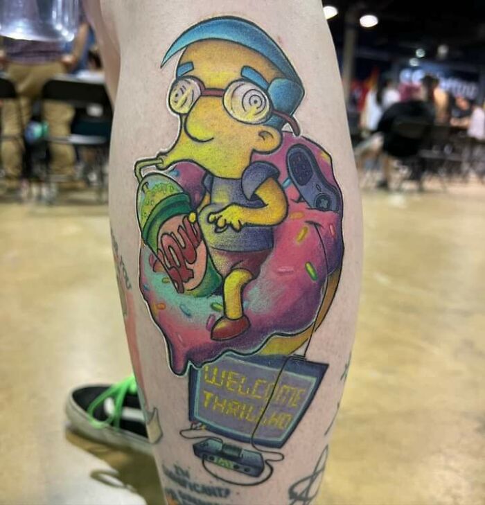 Colorful '90s tattoo of cartoon character with a donut and drink on a person's leg, showcasing decade culture.