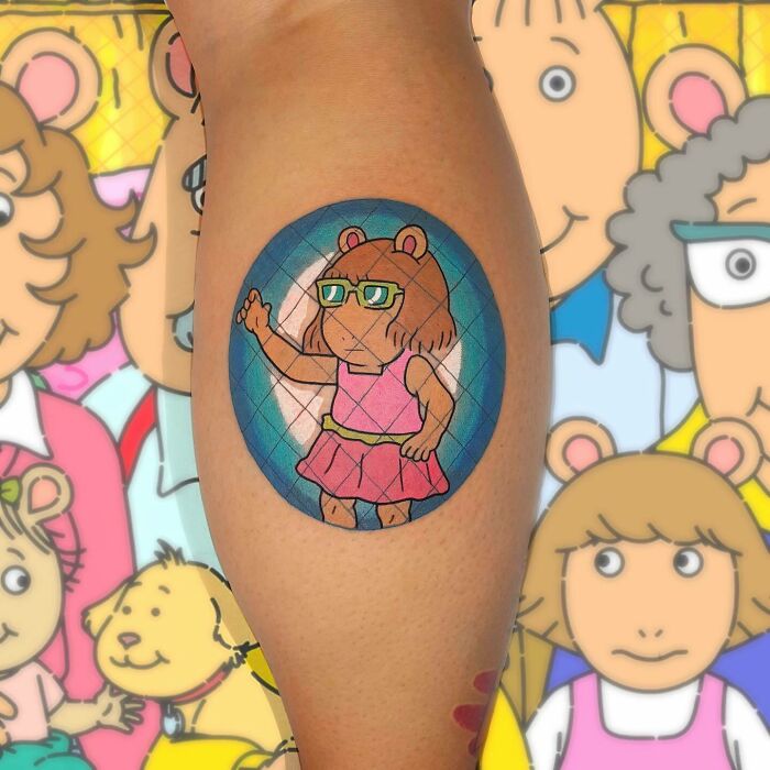 Tattoo of a '90s cartoon bear character wearing glasses and a pink dress on a person's arm, showcasing '90s culture.