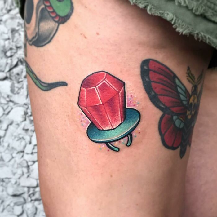 Colorful '90s tattoos featuring a ring pop and butterfly on a thigh, showcasing vibrant nostalgia.
