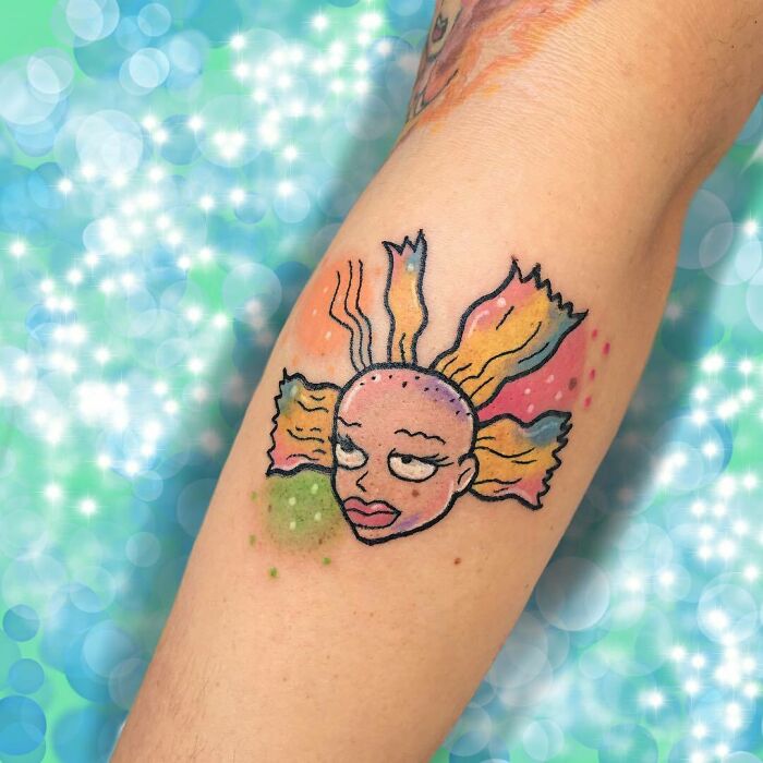Colorful '90s culture tattoo of a cartoon face with colorful hair on an arm.