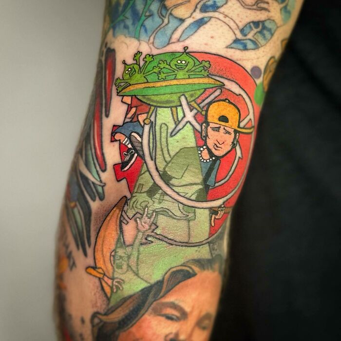 Colorful ‘90s tattoo featuring aliens and a character in a backward cap on an arm.
