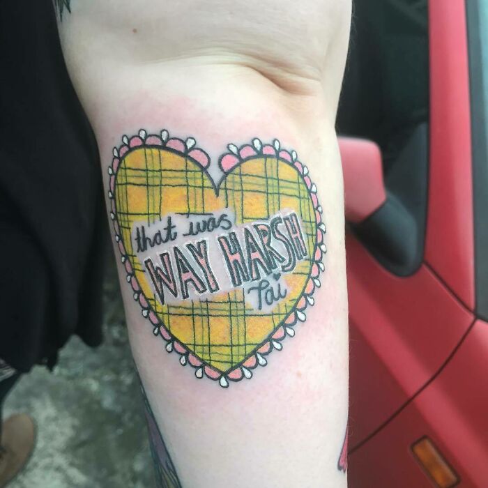 Heart-shaped '90s tattoo with plaid design and text on arm.