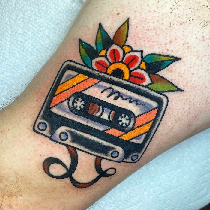 A colorful '90s tattoo of a cassette tape with a flower, showcasing vibrant decade culture.