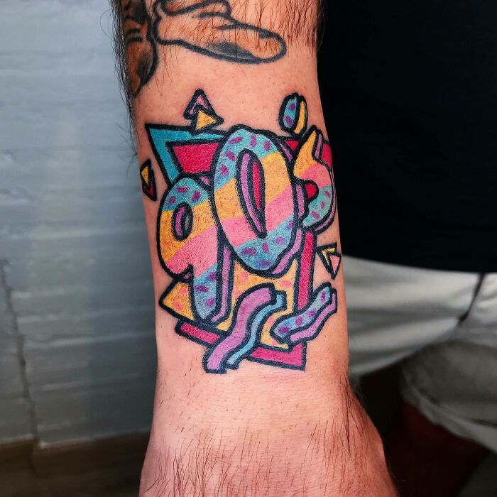 Colorful 90s tattoo with geometric shapes and patterns on a person's forearm, highlighting '90s culture.