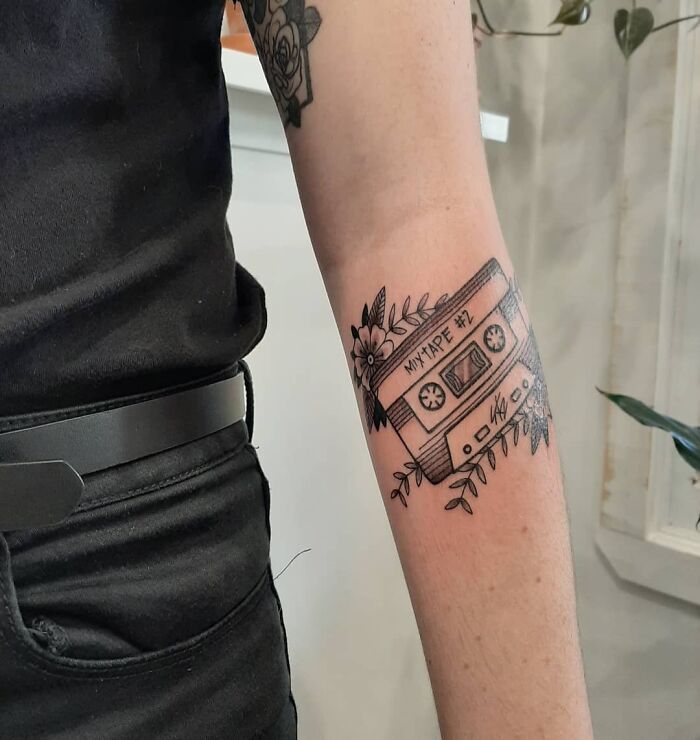 Tattoo of a '90s mixtape with floral details on a person's forearm.