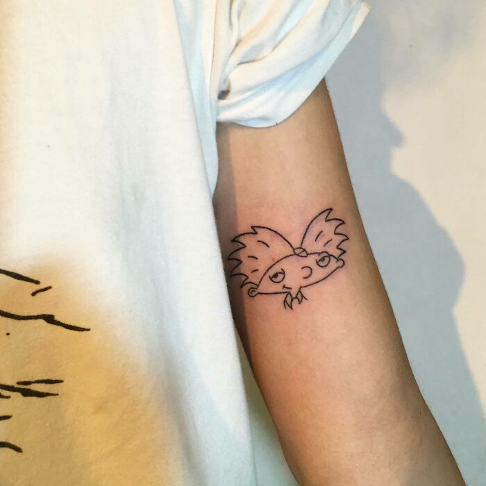 Tattoo of '90s cartoon character on an arm, showcasing decade culture.
