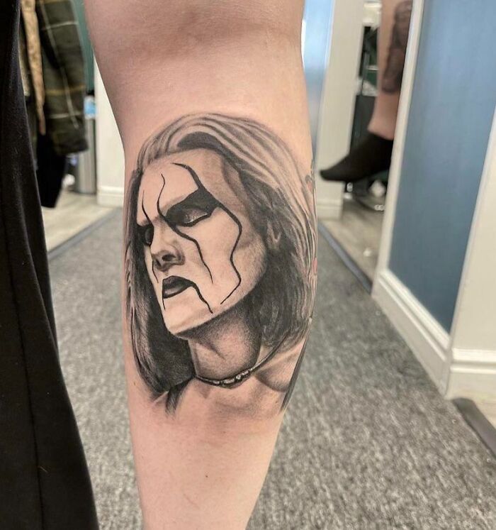 ‘90s tattoo featuring a character with face paint and long hair on a person's arm in a modern setting.