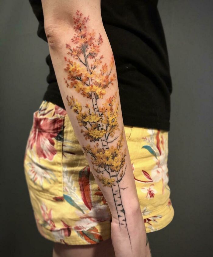 Arm with a colorful tree tattoo, showcasing nature's wonders in intricate detail.