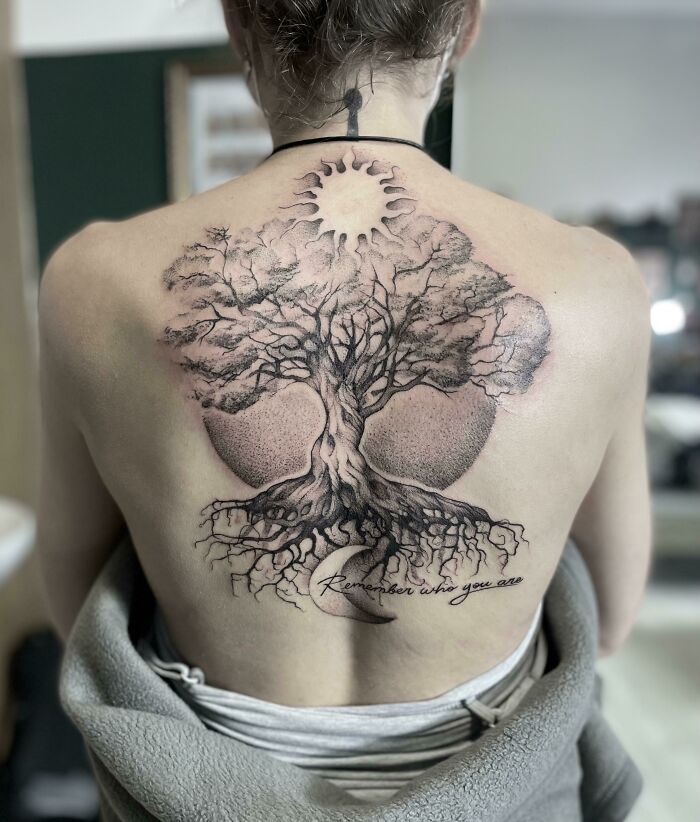 Back tattoo of a majestic tree with roots and branches extending under a sun and moon design.
