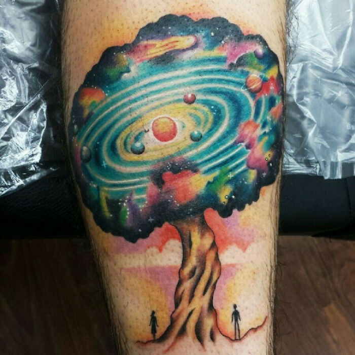 Colorful tree tattoo with cosmic design, featuring planets and galaxies, celebrating nature's wonders.