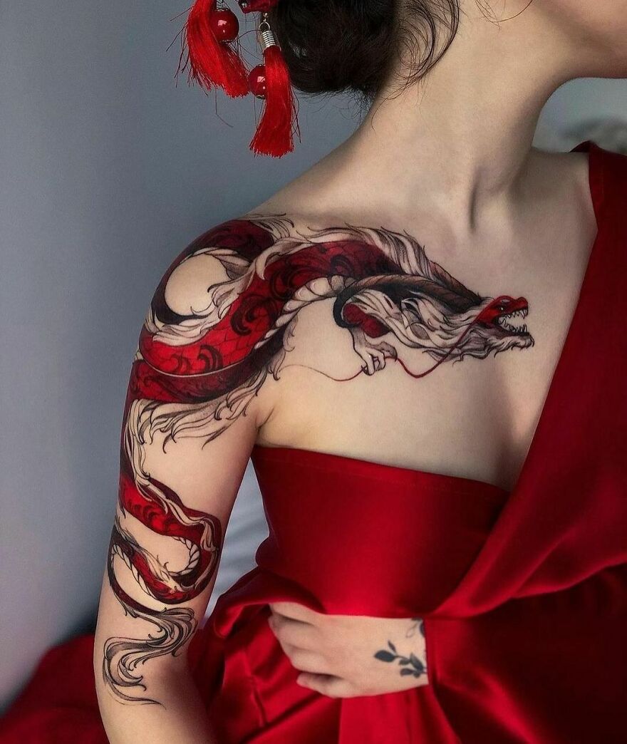 A red and black dragon tattoo on a woman's shoulder, accentuating her red dress, symbolizes fiery strength.