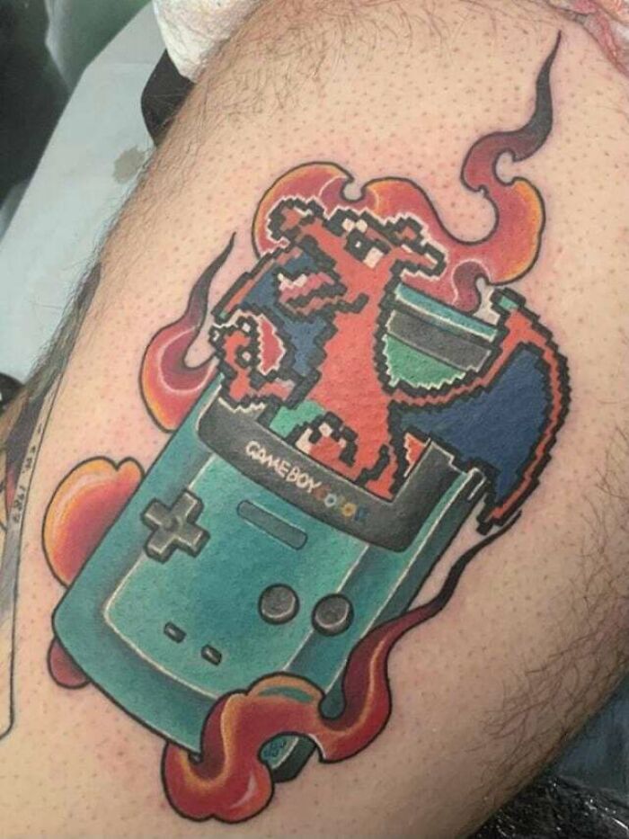 Anime tattoo featuring a pixelated character emerging from a GameBoy with vibrant flames.