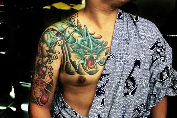 Man with a vibrant anime dragon tattoo across his shoulder and chest, wearing a patterned robe.