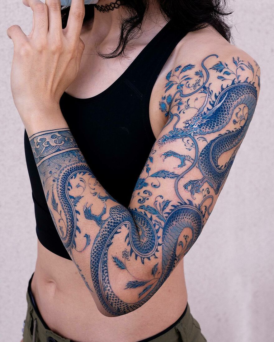 Person with intricate blue dragon tattoo sleeve on arm, showcasing detailed dragon design.