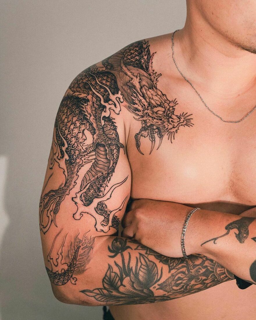 Black dragon tattoo on a man's arm and shoulder, showcasing intricate designs and bold lines.