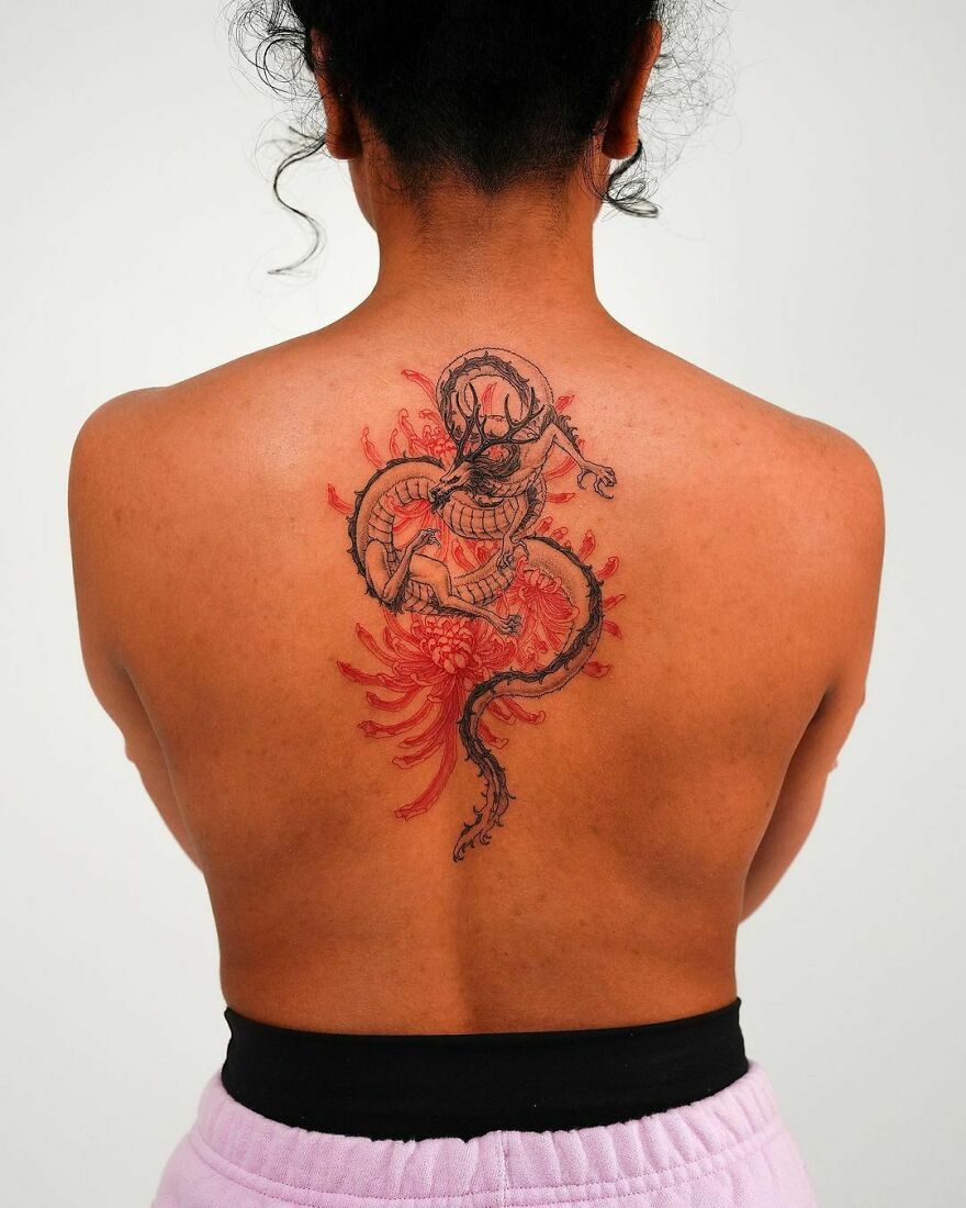 Person with detailed dragon tattoo on their back, featuring red and black ink accents.