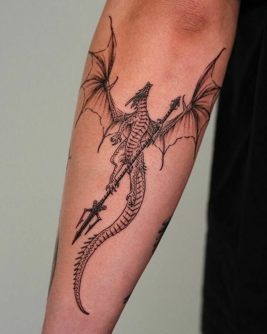 Dragon tattoo design with spear on forearm, showcasing intricate wing and tail details.