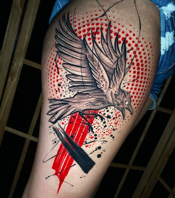 Trash Polka tattoo of a crow with red and black abstract elements on a person's thigh.