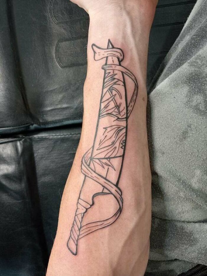 Anime tattoo featuring a stylized sword design on a person's forearm.