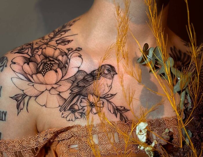 Collarbone tattoo featuring a detailed floral and bird design on a woman's shoulder, framed by delicate foliage.