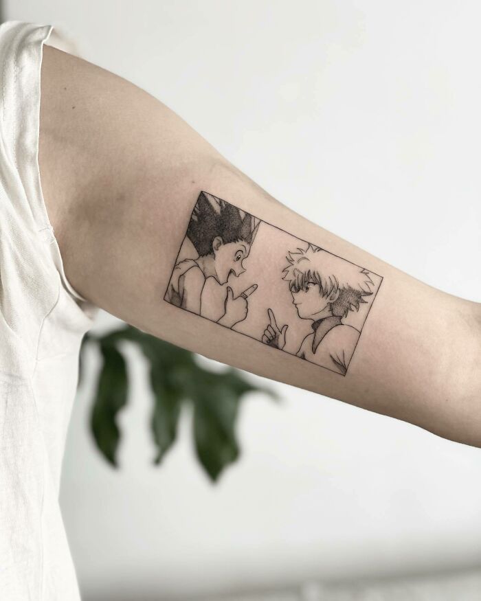 Anime tattoo of two characters in profile with pointed fingers on a person's arm.