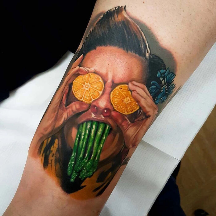 A colorful '90s tattoo featuring a surreal face with orange slices as eyes and asparagus coming from the mouth.