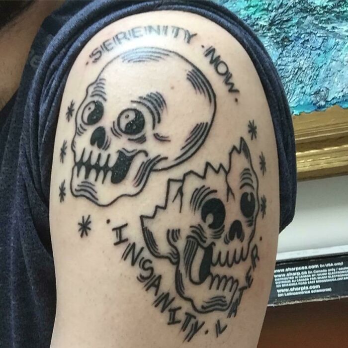'90s tattoo with skulls and text "Serenity Now, Insanity Later" on upper arm.