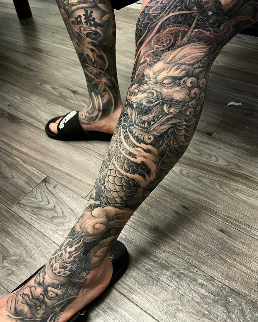 Detailed black and gray dragon tattoo covering a leg, featuring scales and fierce eyes.