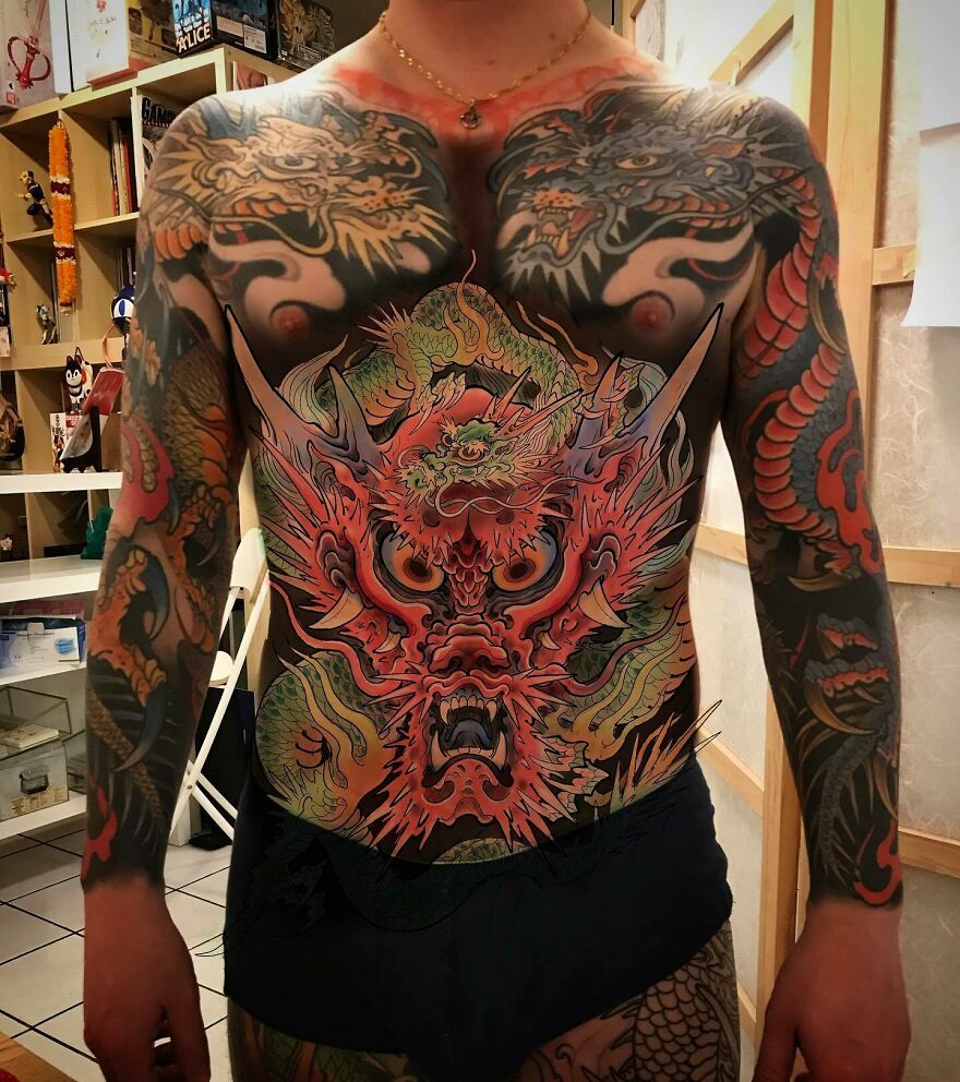Colorful dragon tattoo covering a person's chest and arms, showcasing intricate designs and vibrant hues.