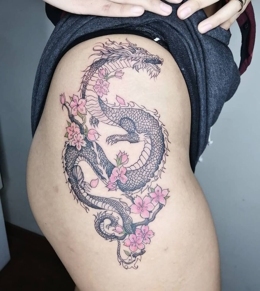 Dragon tattoo design with pink flowers on a person's thigh.