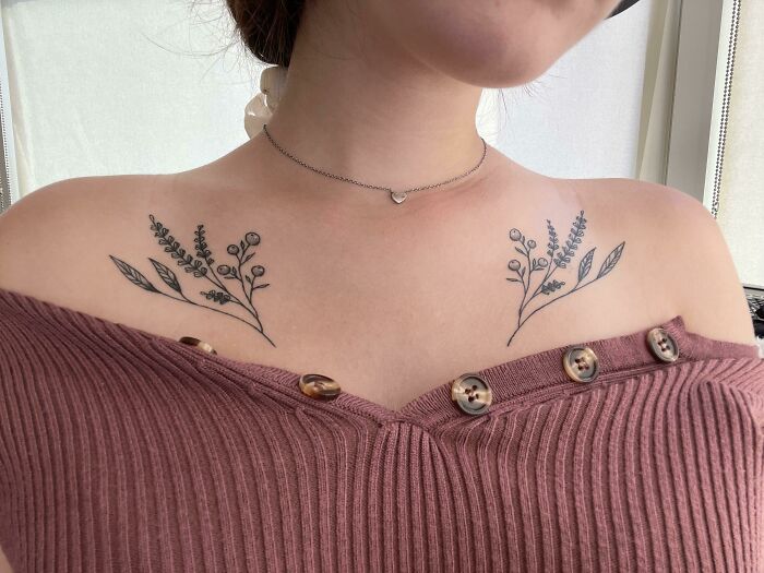 Delicate collarbone tattoos featuring floral designs on a person wearing a maroon top.