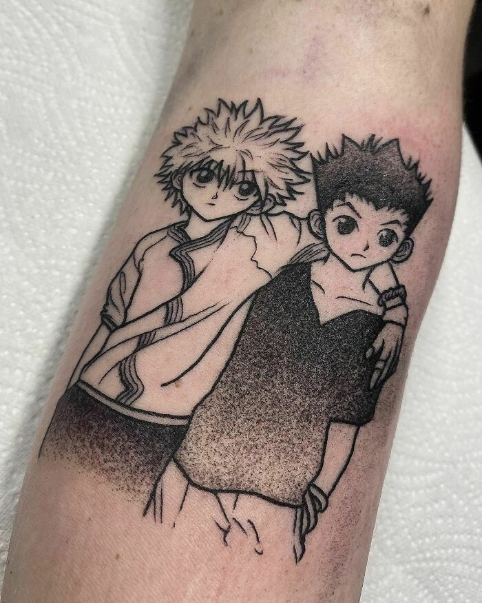Anime tattoo of two characters with arms around each other, showcasing detailed black linework on forearm.
