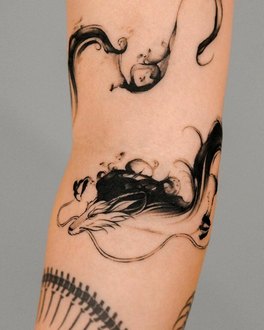 Artistic dragon tattoo on forearm, showcasing flowing black ink design.