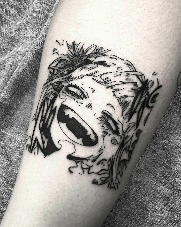 Stylized anime tattoo on skin, featuring a character's expressive, laughing face.