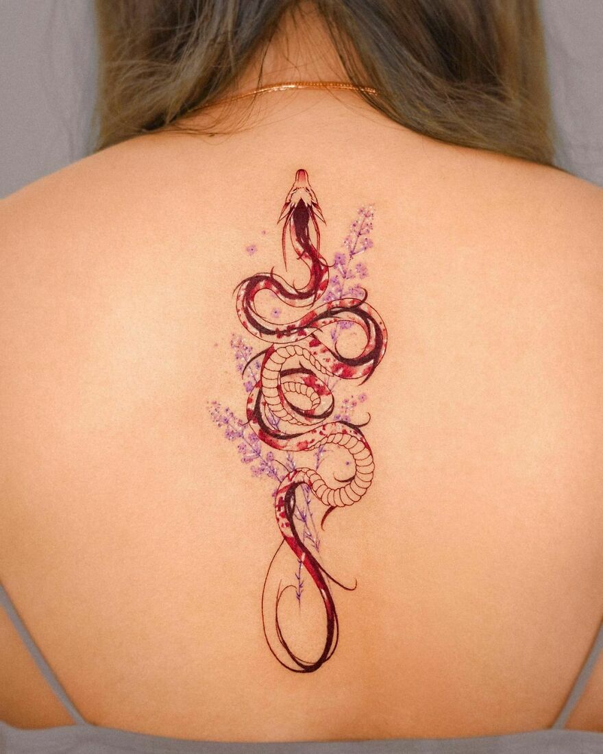 Intricate red dragon tattoo design on woman's back with floral accents.