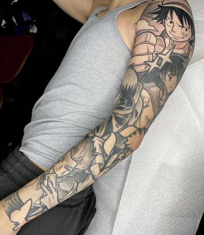 Arm with intricate anime tattoo sleeves featuring popular characters, showcasing detailed and cool designs in black ink.