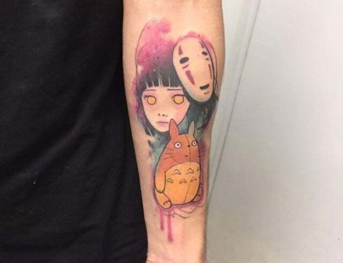 Anime tattoo featuring colorful Miyazaki-inspired characters on a forearm.