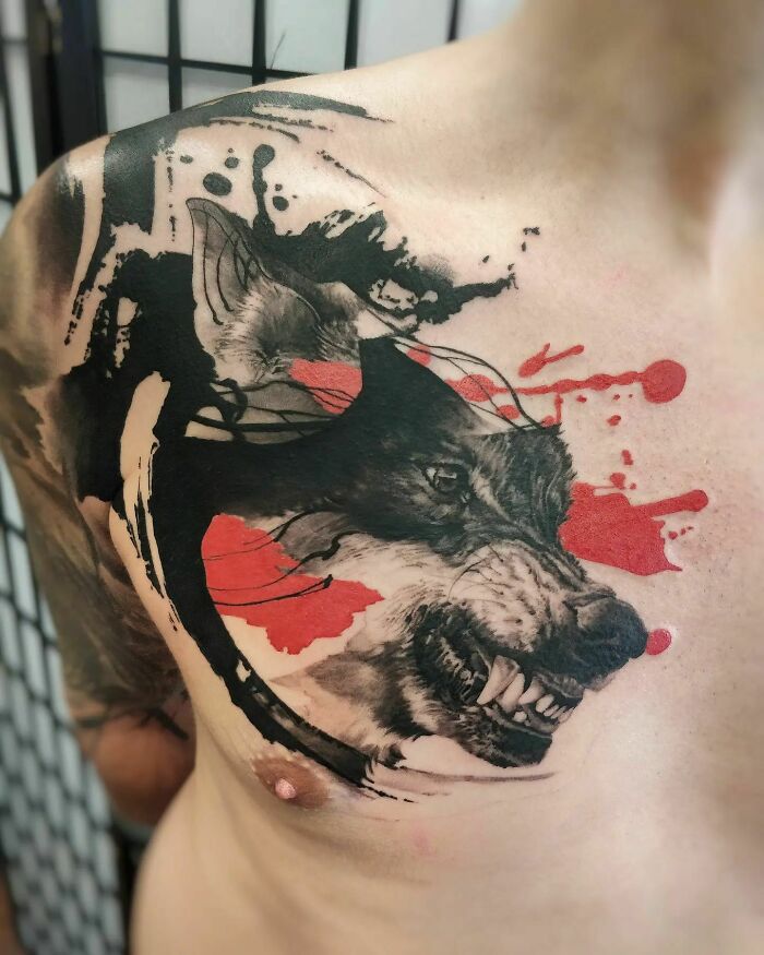 Trash Polka tattoo of a wolf on a person's chest, featuring bold black and red ink splashes.