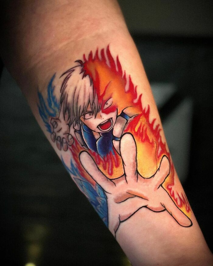 Anime tattoo featuring a dynamic character design with vibrant red and blue flames on a forearm.