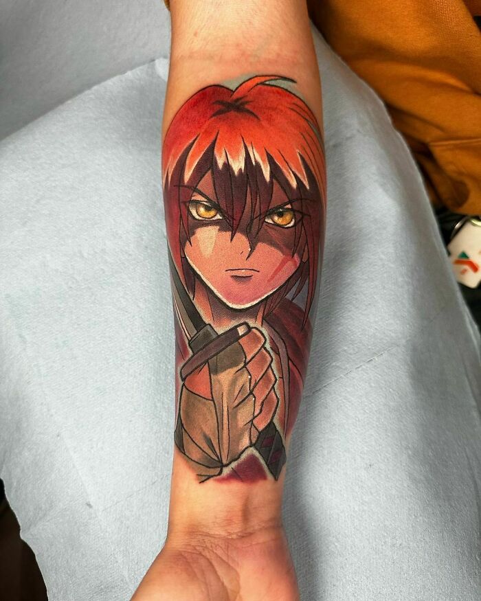 Anime tattoo of a red-haired character with intense eyes, holding a sword, on a forearm.