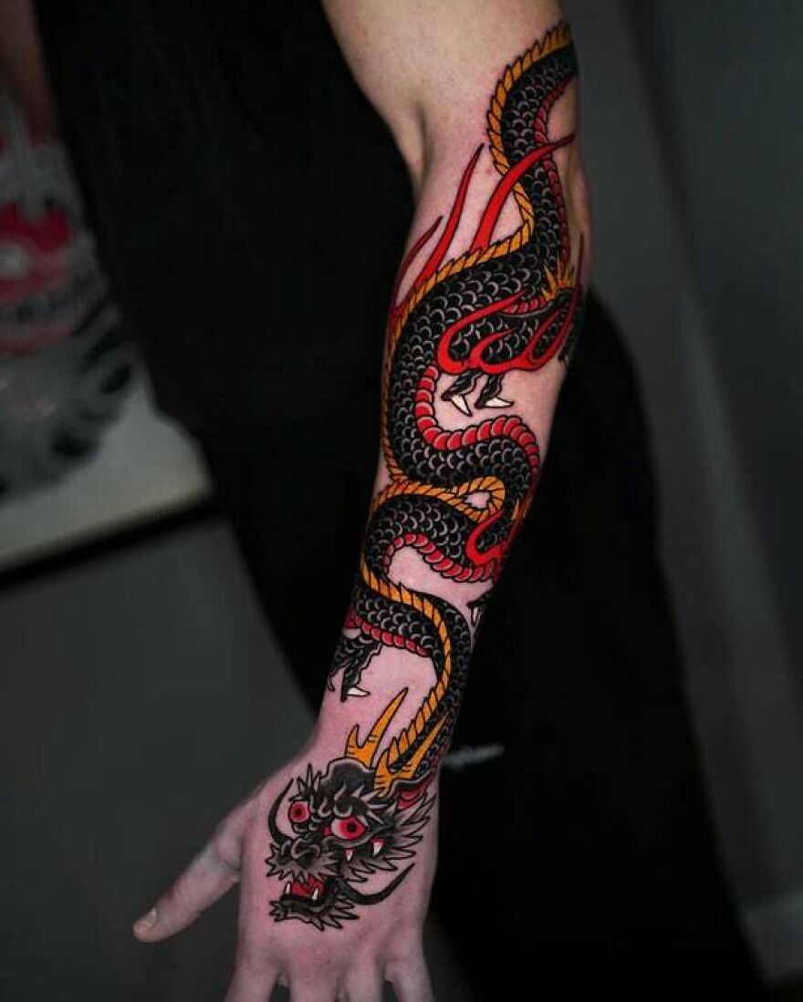 Arm with vibrant dragon tattoo in black, red, and yellow hues.