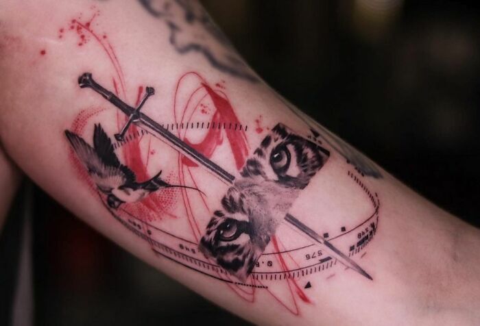 Detailed Trash Polka tattoo featuring a sword, bird, and intense eyes with red accents on an arm.