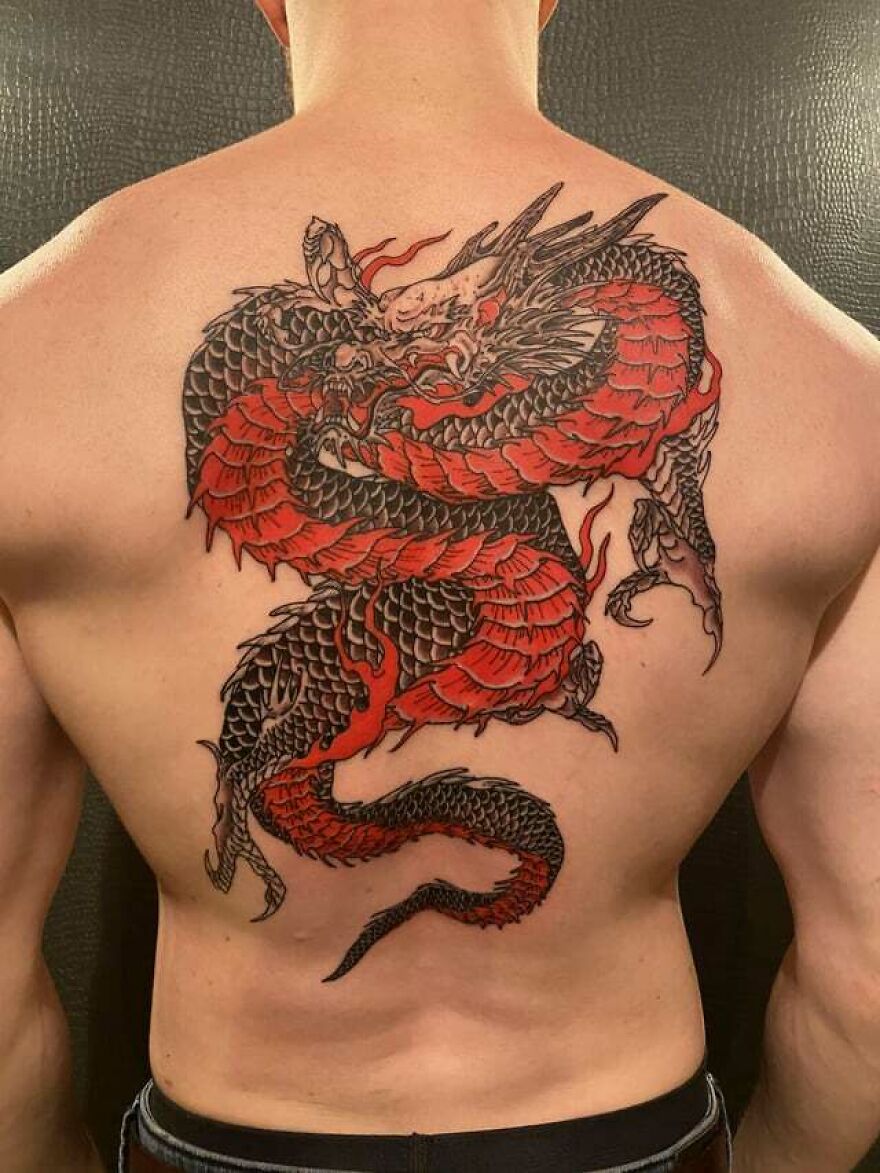 Red and black dragon tattoo on a person's back, showcasing intricate design and bold colors.