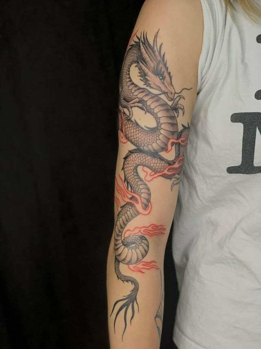 Detailed dragon tattoo on person's arm, featuring red flames and intricate scales.