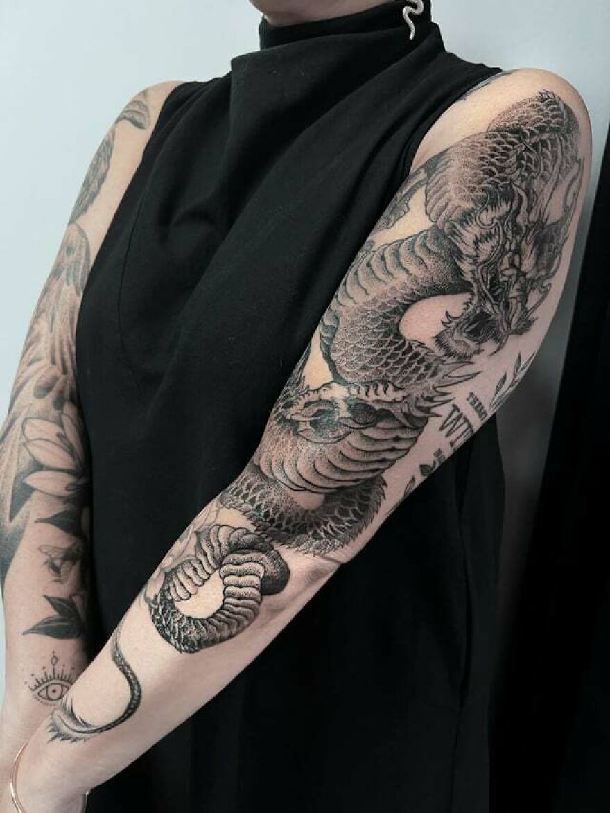 Dragon tattoo covering a person's arm, featuring intricate scales and fierce details.